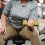 Kobieta plus size w legginsach siedzi na ławce i ćwiczy bicepsy hantlami
