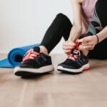 Kobieta wiąże buty sportowe na macie obok hantli przed treningiem