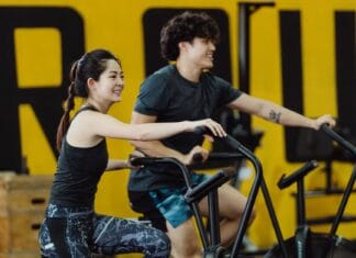 Jak nagradzać się za postępy w sporcie, nie sabotując diety i wypracowanych nawyków ruchowych Uśmiechnięta para ćwiczy na rowerach stacjonarnych na siłowni