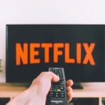 Dłoń z pilotem skierowana w stronę ekranu telewizora z Netflix