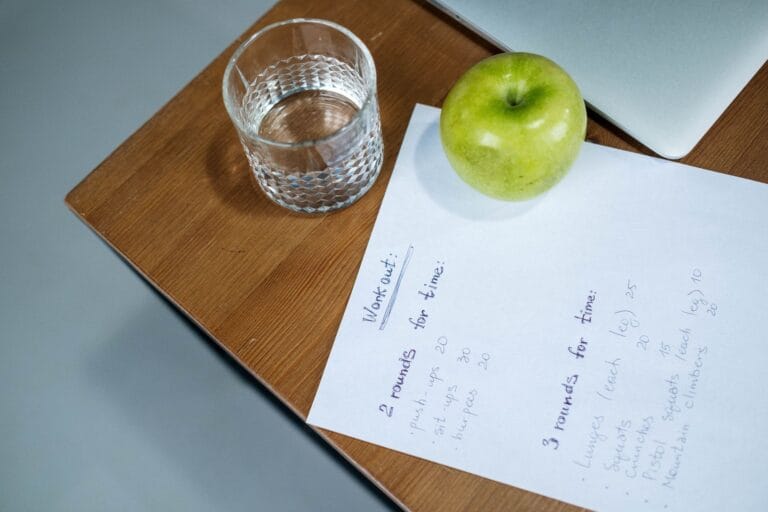 Jabłko, woda i plan treningowy na drewnianym biurku